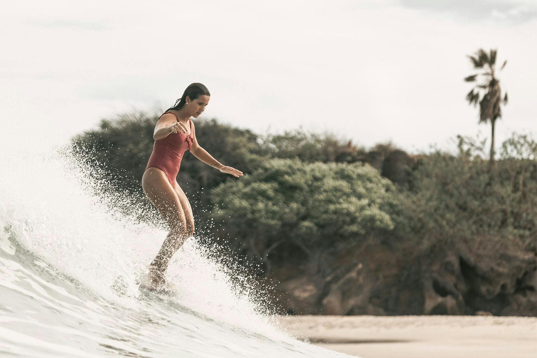 female longboard surfer noseriding with a tropical jungle in the background, by ana catarina