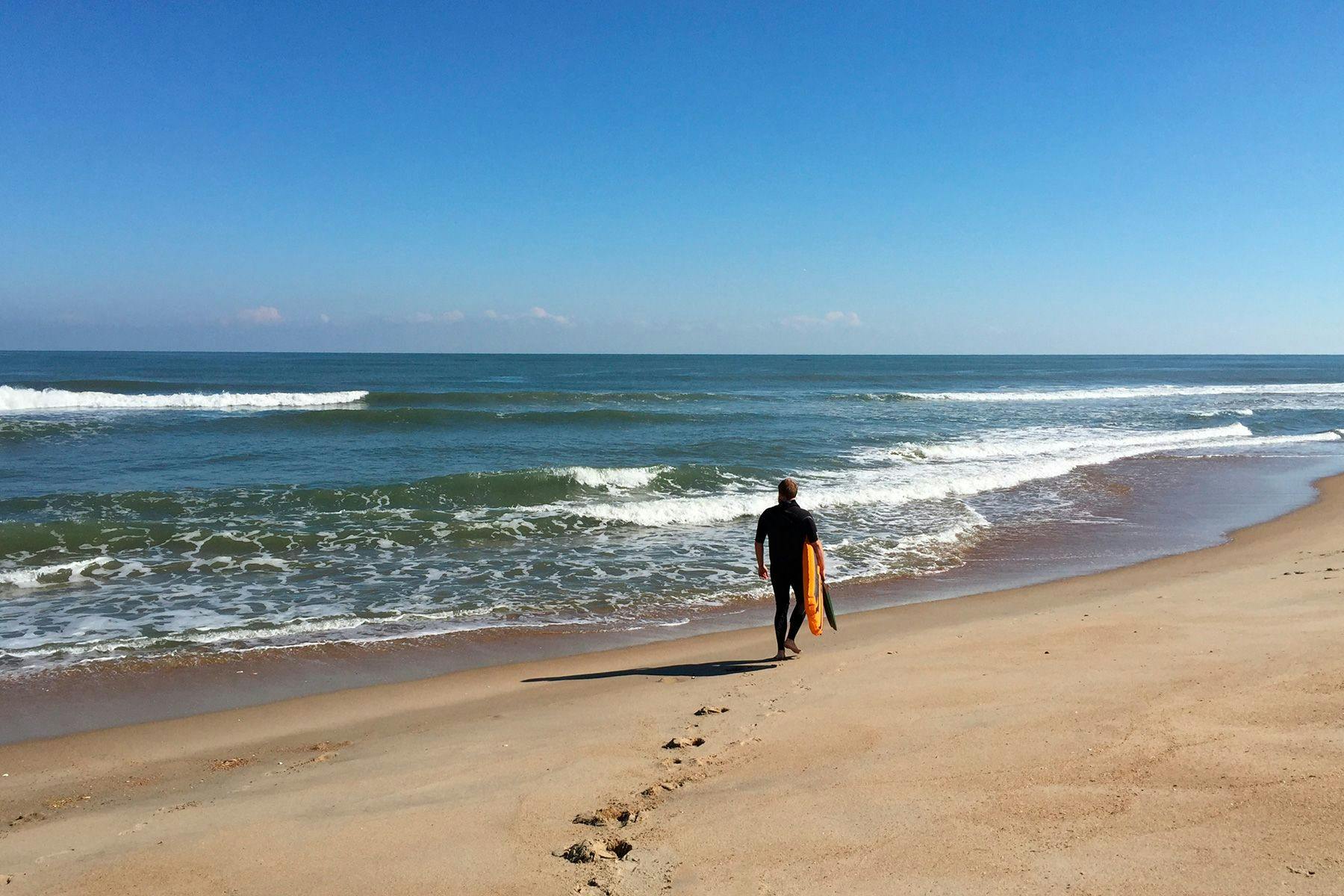 Jamie McClellan carries his surfmat along a deserted Cape Hatteras beach. Photographed by Tatum Clements.