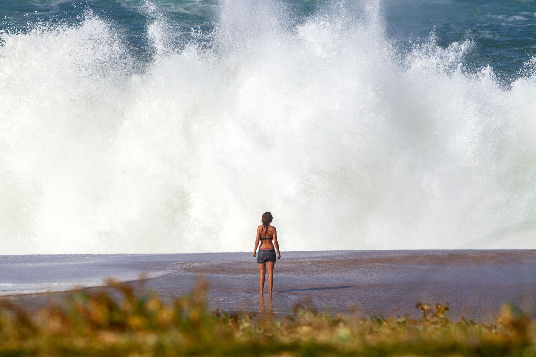 woman standing on the beach in front of a large breaking wave