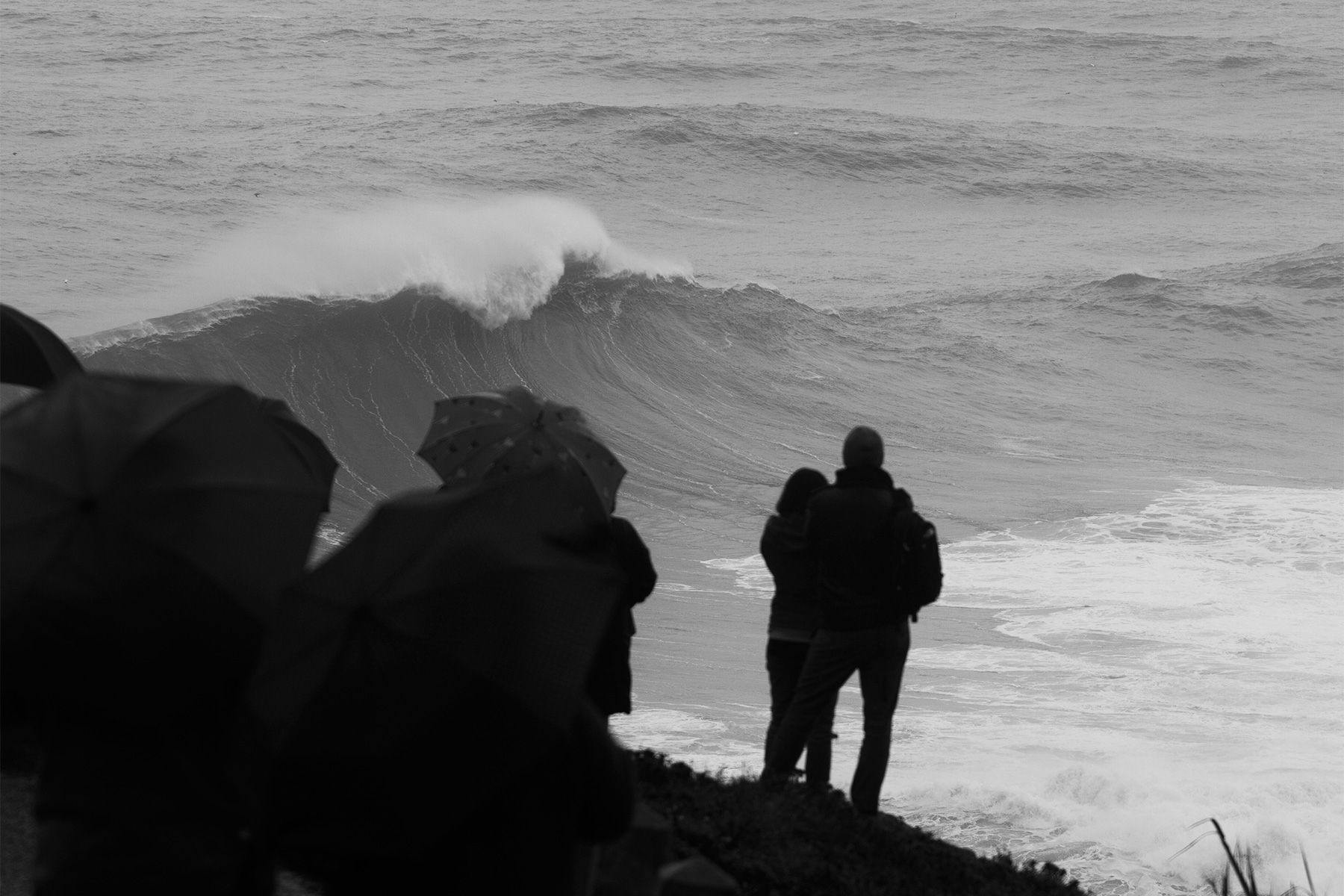 A couple stand and watch waves break at nazare in portugal