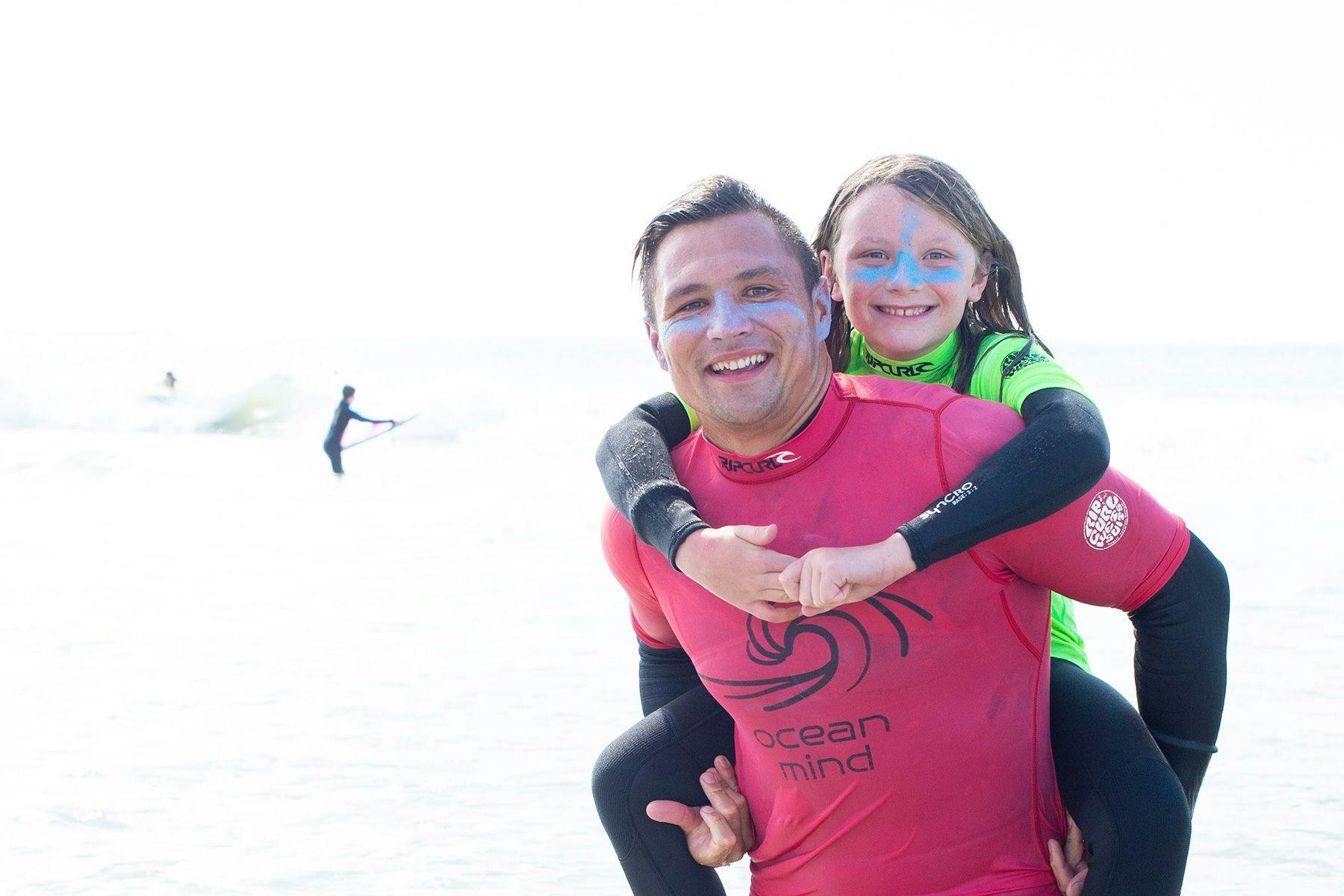 ocean mind surf coach giving a student a piggy-back in the sea