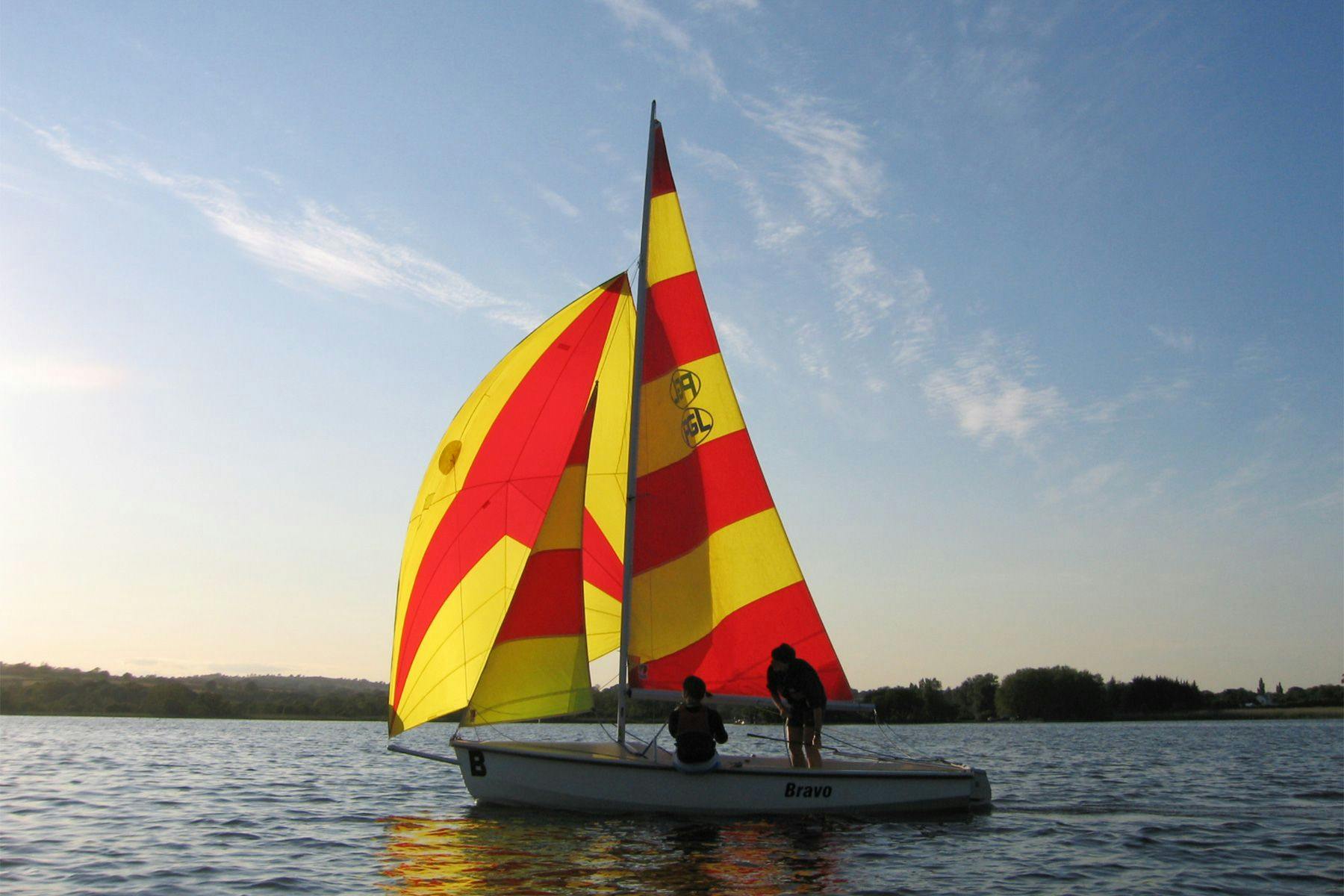 sailing a dinghy with backlit red and yellow sails and a spinnaker