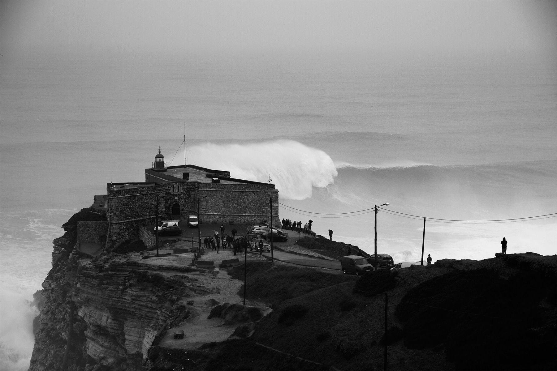 a huge wave breaking in front of the lighthouse at nazare in portugal