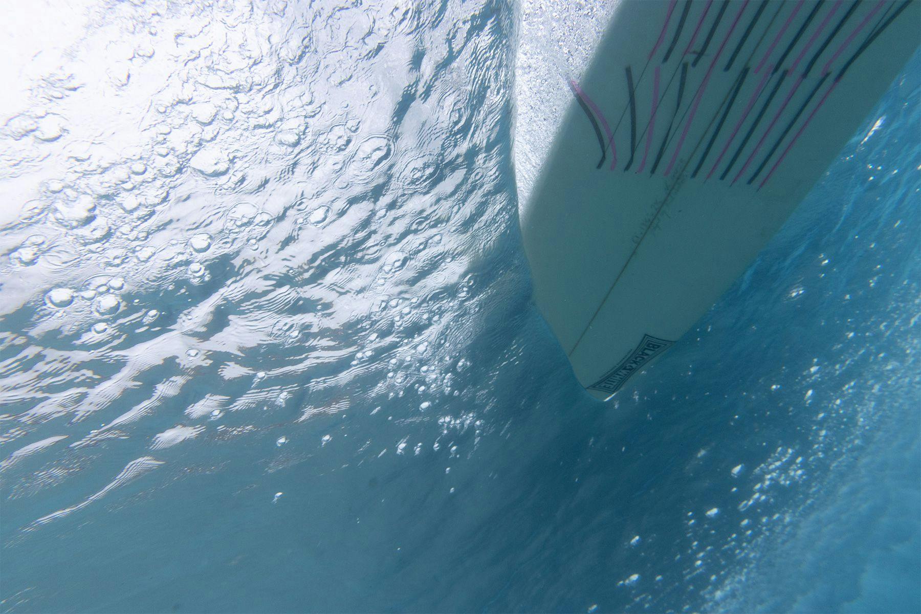 underwater photo showing the shear flow of water off the edge of the underside of a surfboard going along a wave