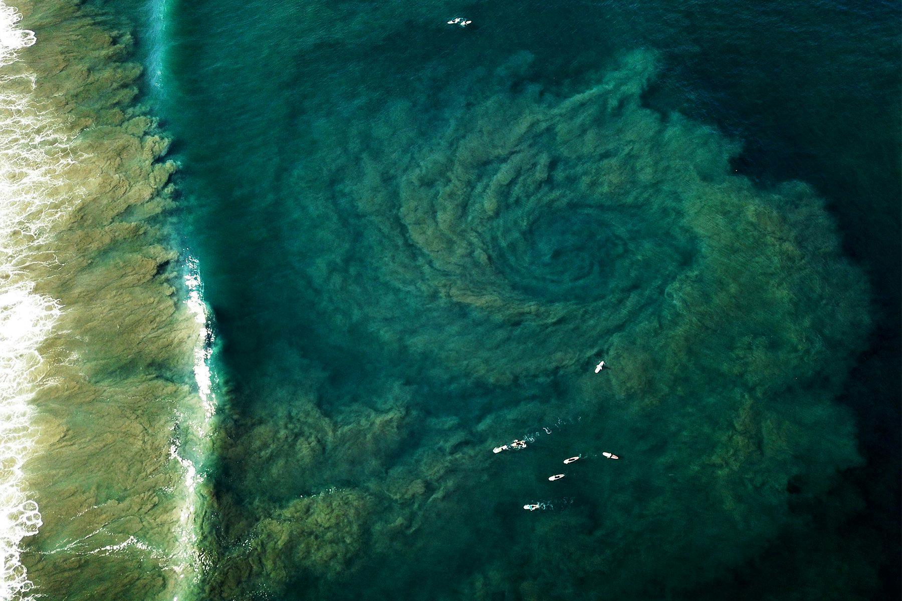 aerial drone photograph of surfers and a rip plume at playa guiones in costa rica