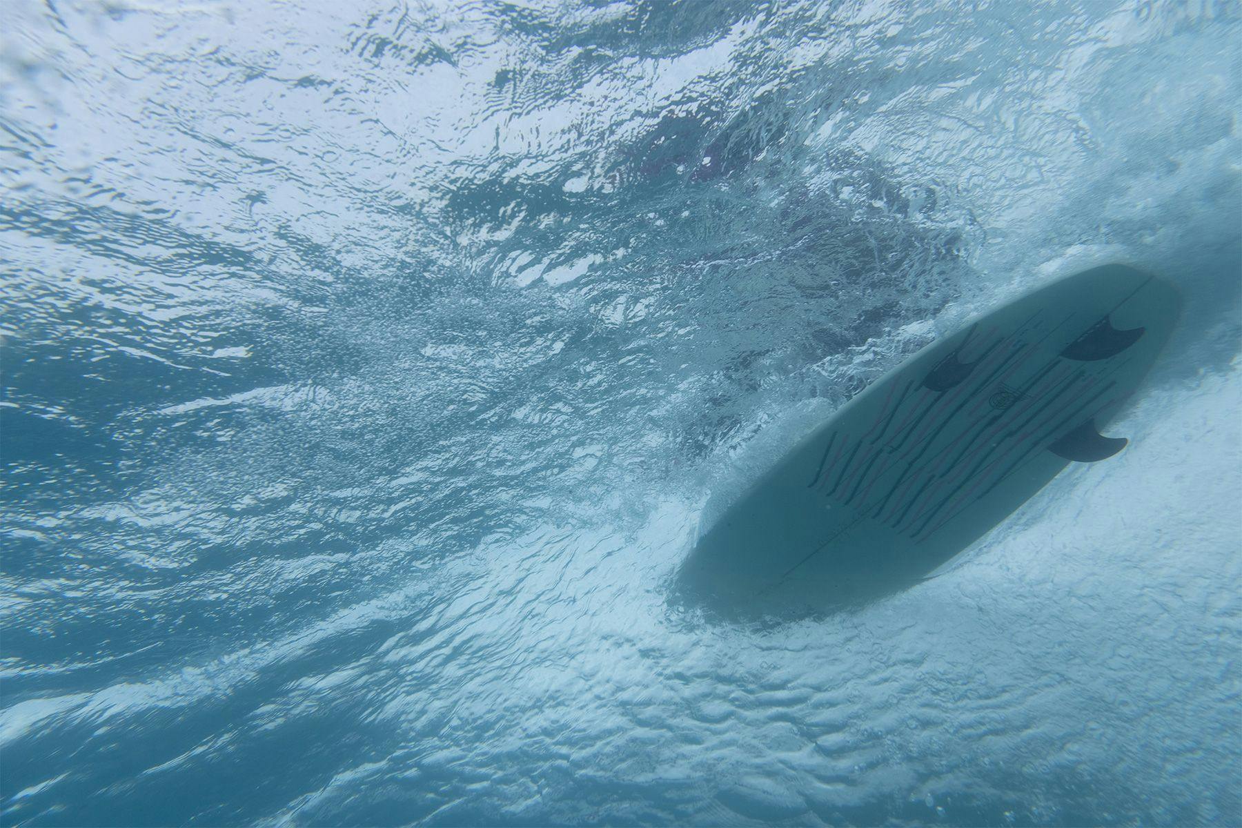 underwater view of a surfboard going along a wave with telltale ribbons showing the flow of water