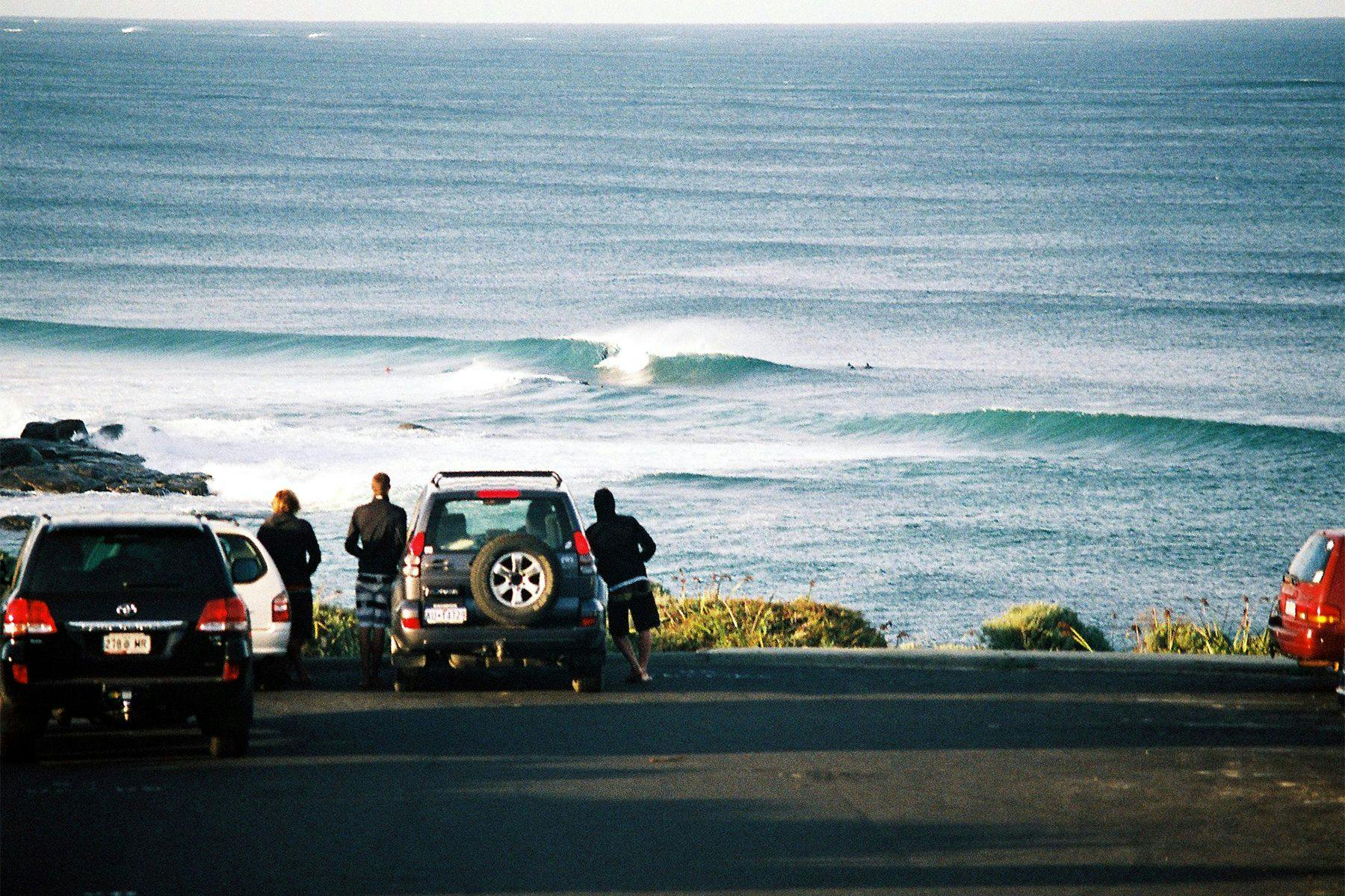 surfers leaning on a car in a car park watching the waves