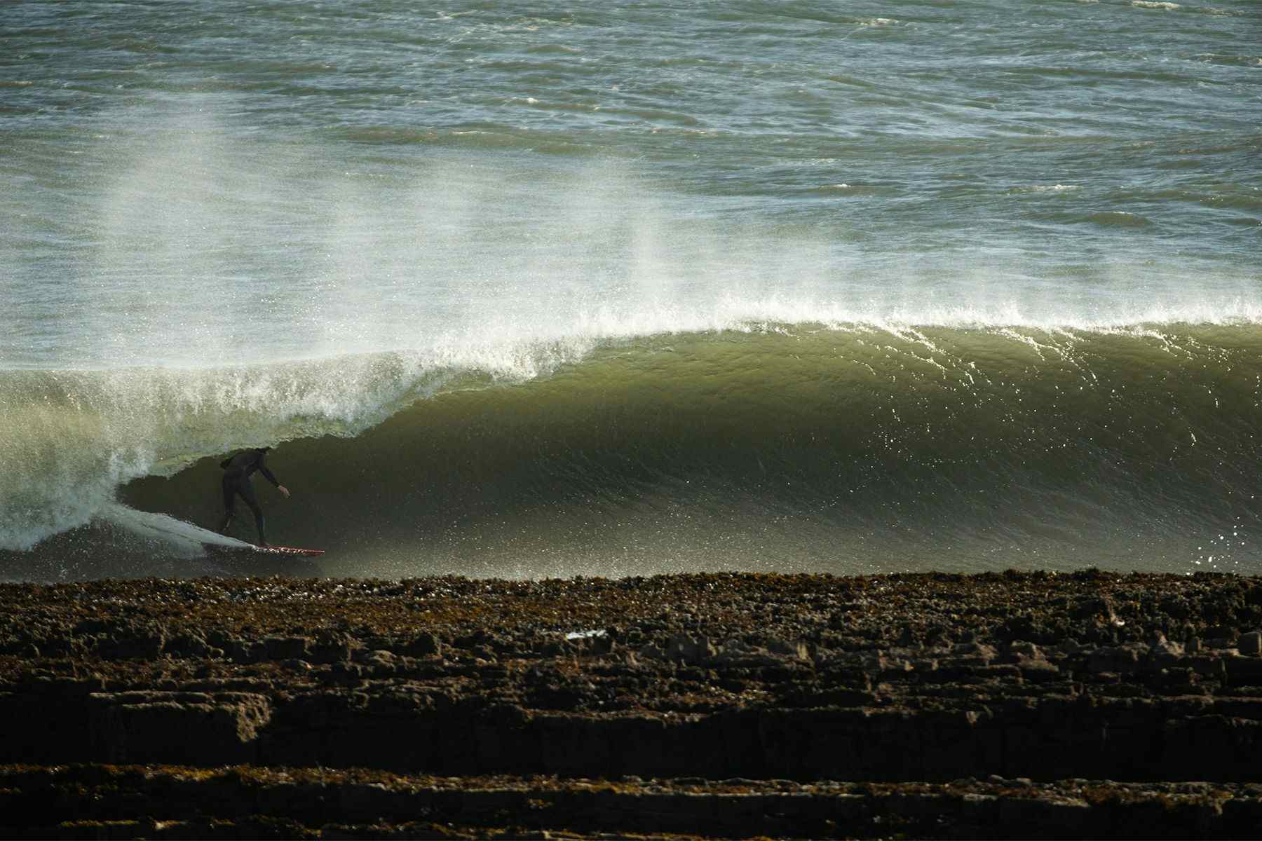 surfer noah lane on a barrelling left hand wave, surfing wearing a natural rubber wetsuit