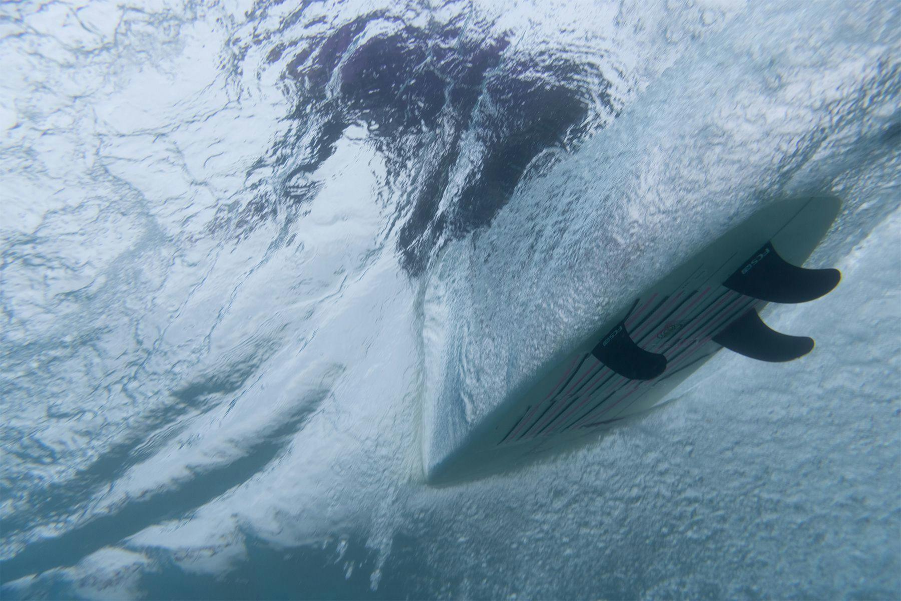 underwater view of a surfboard with telltale ribbons showing the flow of water and fluid dynamics across the underside of the surfboard