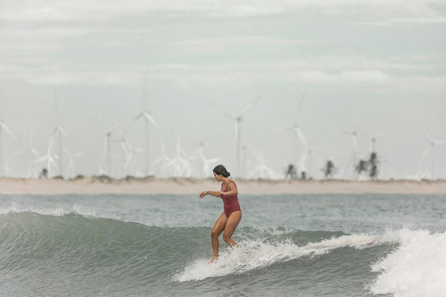 female longboard surfer noseriding a wave in brazil with a wind farm in the background