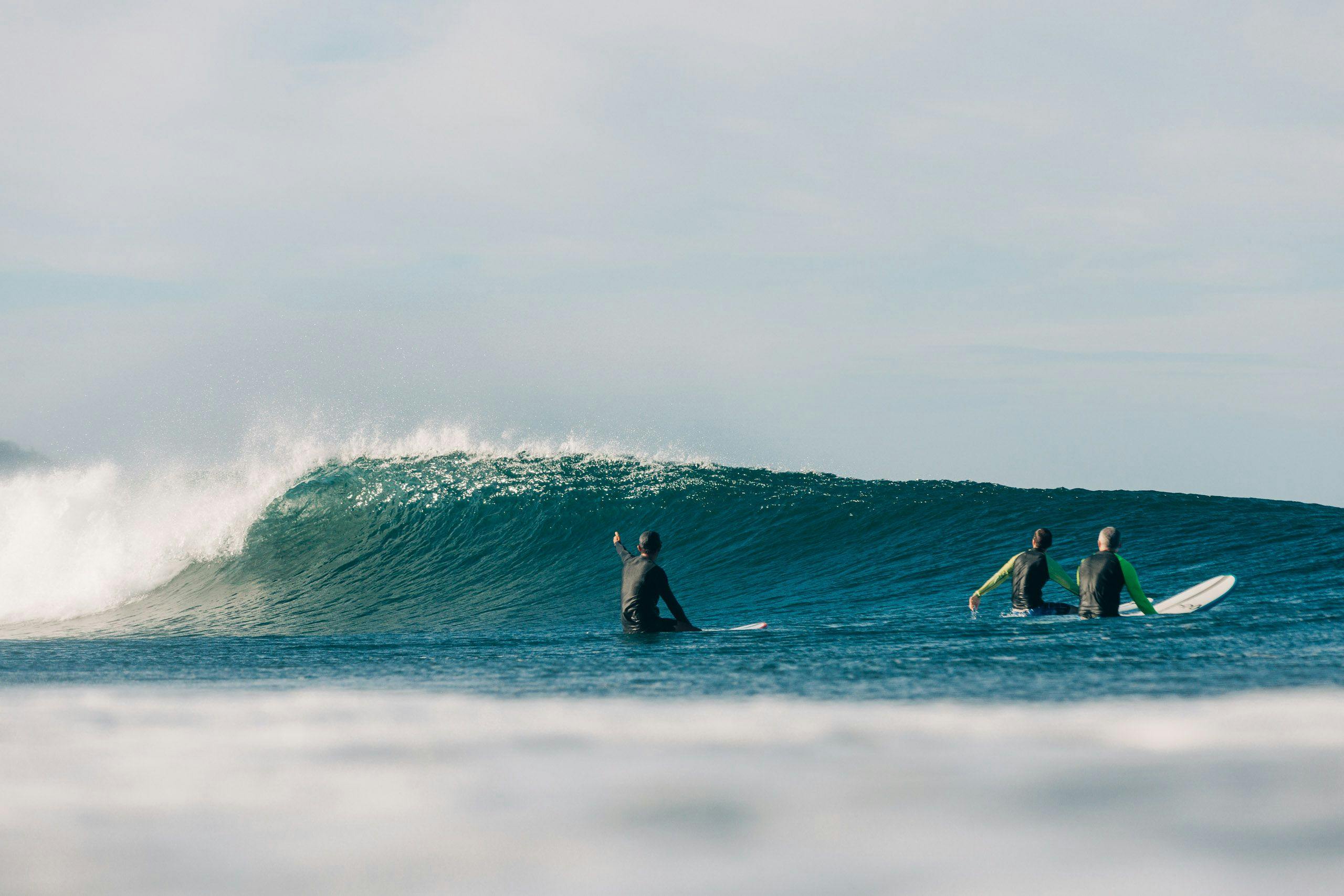 surfers sitting on their boards watching a wave break at surf simply in costa rica