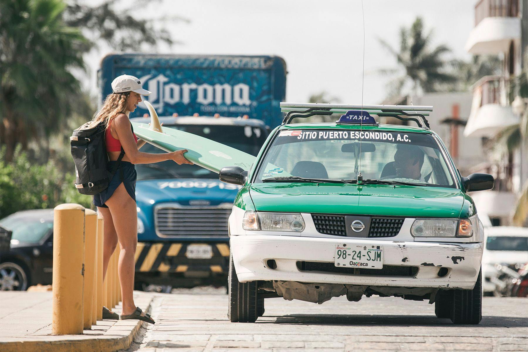 surfer loading her surfboard into a taxi in puerto excondido in mexico, by ana catarina