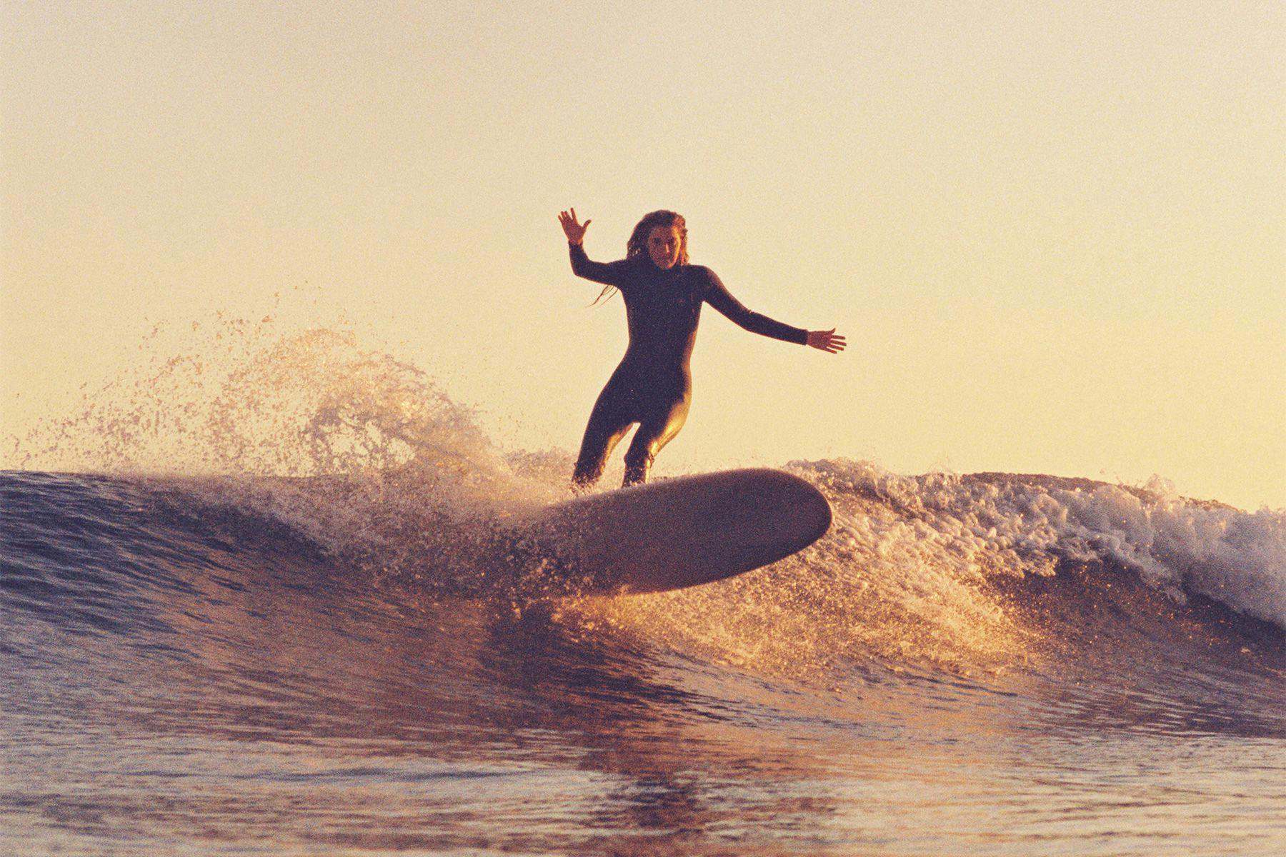 woman on a longboard surfboard cutting back at malibu in golden evening light, shot on a nikonos film camera by grant musso