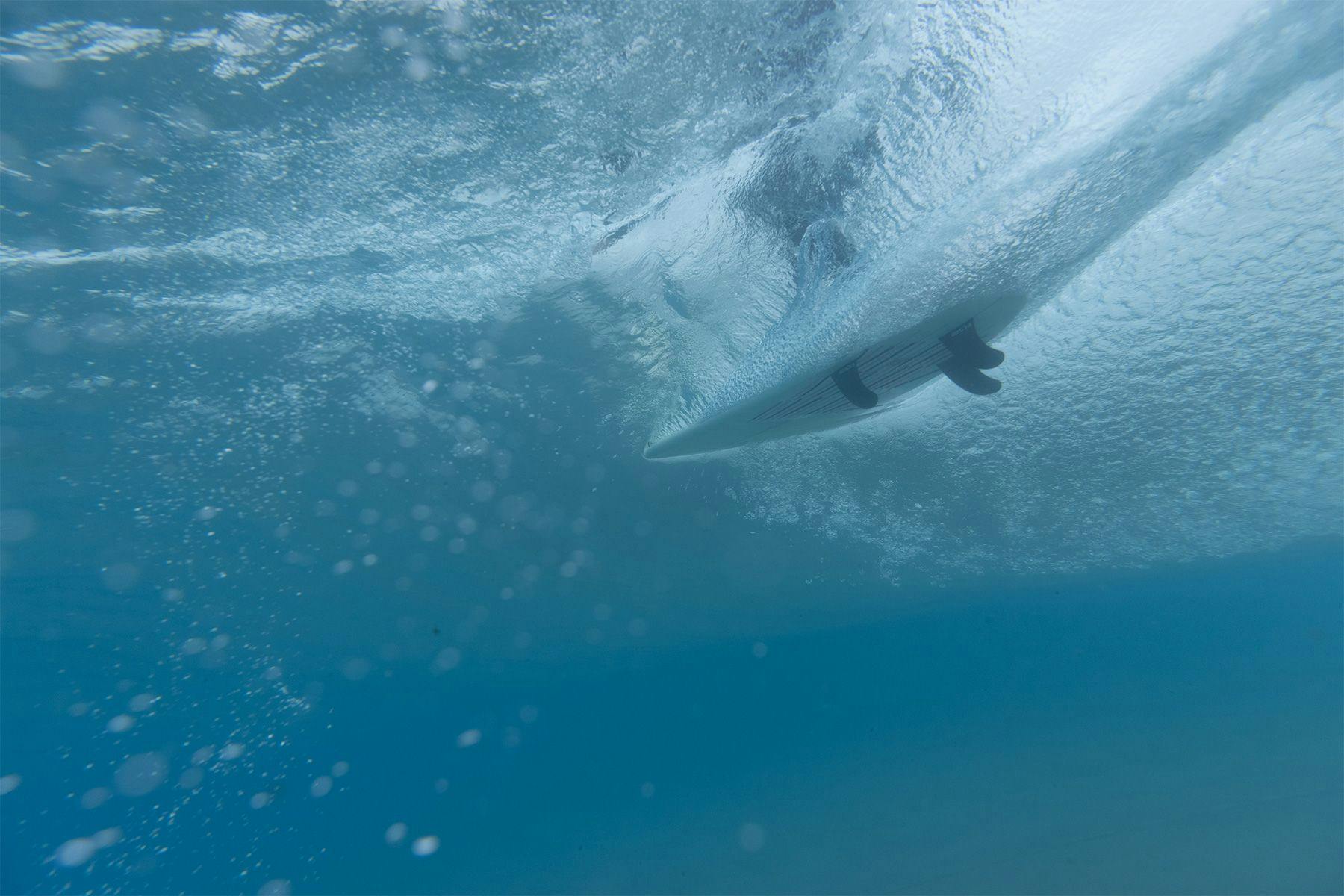 a surfboard travelling along a wave as see from underwater