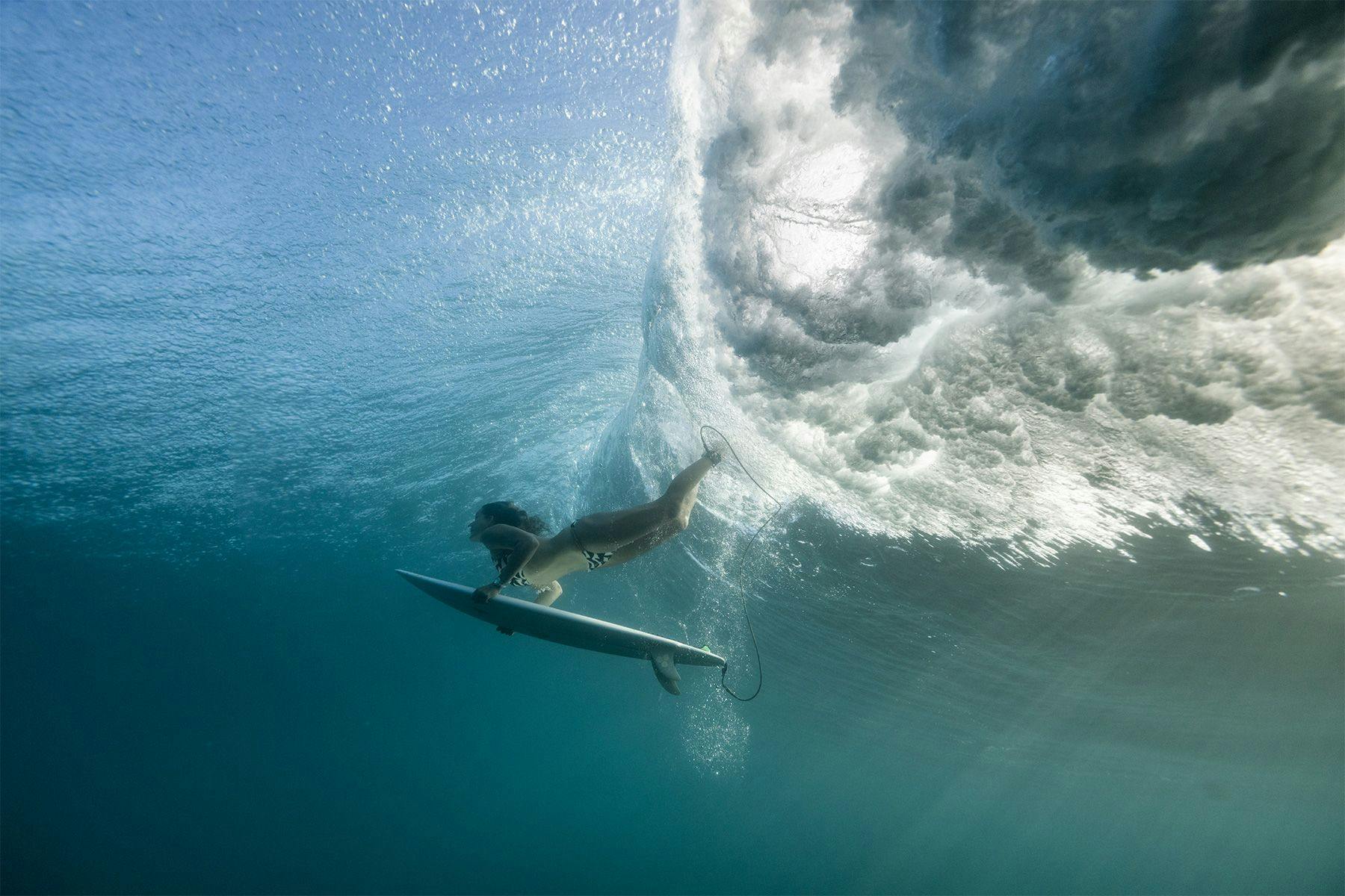 female surfer duck diving under a wave in the tropic, by ana catarina